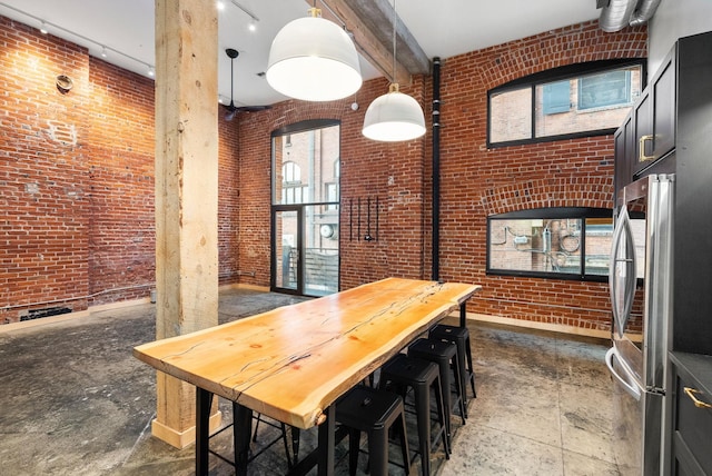 dining area with brick wall, baseboards, concrete floors, and a towering ceiling