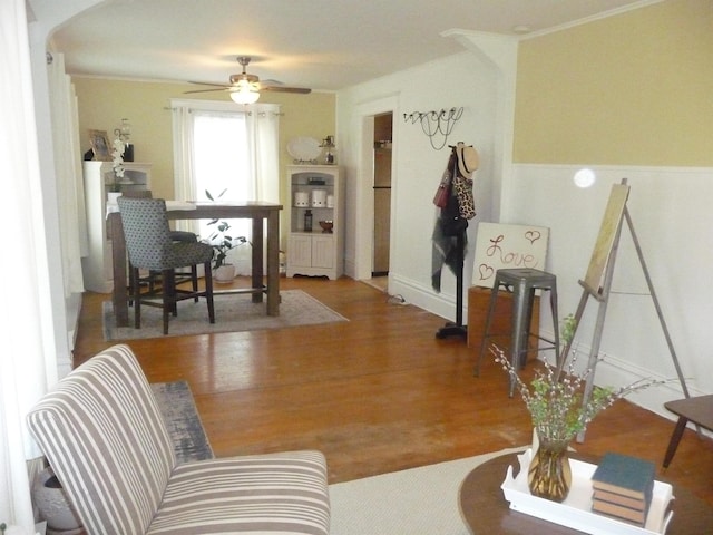 living area with wood finished floors, ceiling fan, arched walkways, and wainscoting
