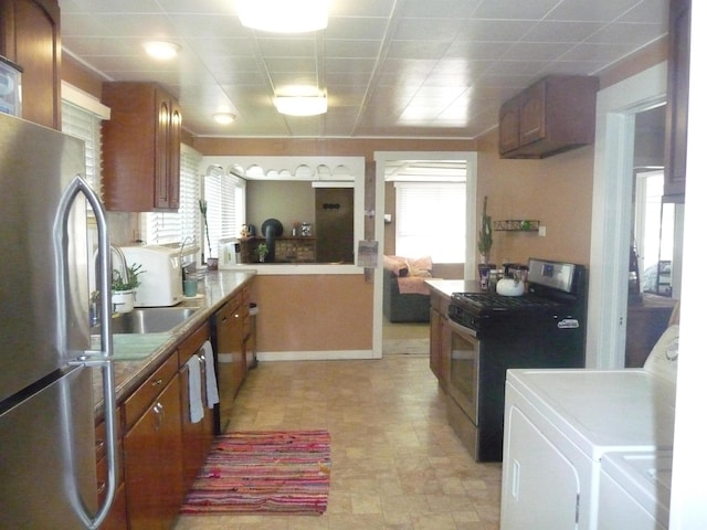 kitchen featuring appliances with stainless steel finishes, washing machine and dryer, brown cabinetry, a sink, and plenty of natural light