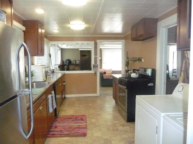 kitchen featuring appliances with stainless steel finishes, washing machine and clothes dryer, brown cabinetry, baseboards, and healthy amount of natural light