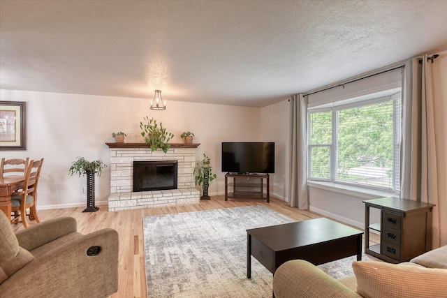 living area with light wood-type flooring, a textured ceiling, baseboards, and a stone fireplace