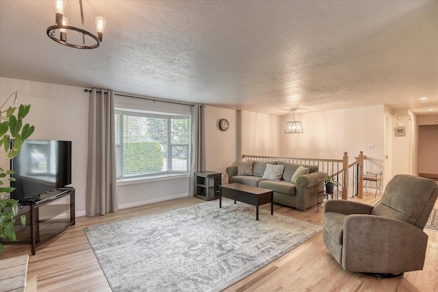 living area featuring a chandelier, a textured ceiling, light wood-type flooring, and baseboards