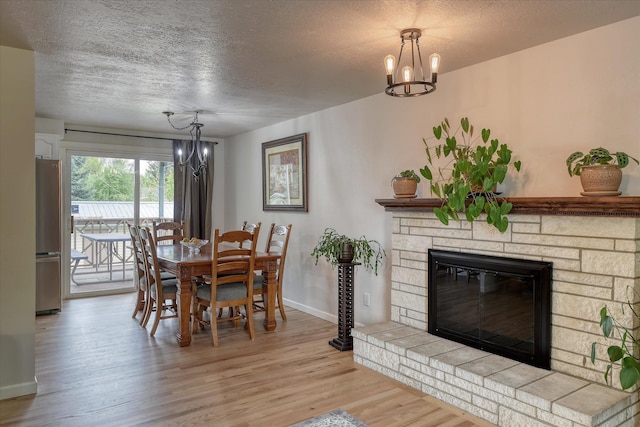 dining area featuring a chandelier, light wood-type flooring, baseboards, a textured ceiling, and a fireplace