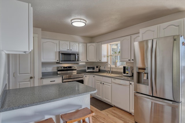 kitchen featuring appliances with stainless steel finishes, a sink, white cabinets, a breakfast bar, and a textured ceiling
