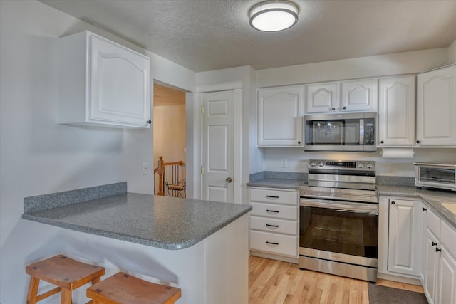 kitchen with appliances with stainless steel finishes, a peninsula, a kitchen bar, white cabinets, and light wood finished floors