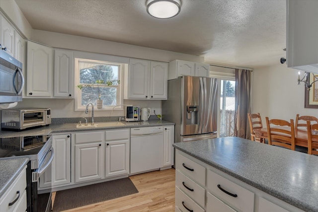 kitchen featuring stainless steel appliances, a sink, a textured ceiling, light wood-style floors, and white cabinets