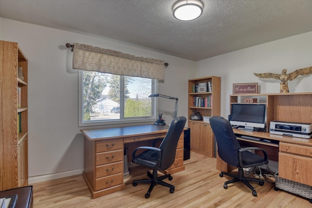 home office with light wood-style floors, a textured ceiling, and baseboards
