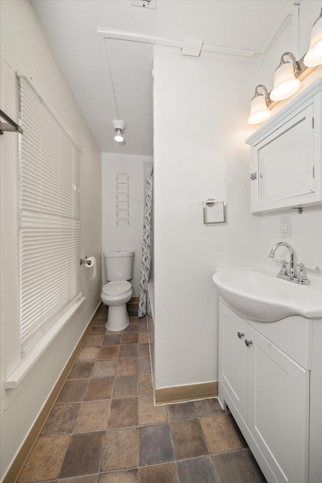 1207 E Wabash Ave, Spokane, WA 99207 - bathroom featuring baseboards, stone finish floors, toilet, and vanity