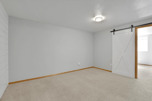 carpeted spare room with baseboards, a barn door, and a textured ceiling