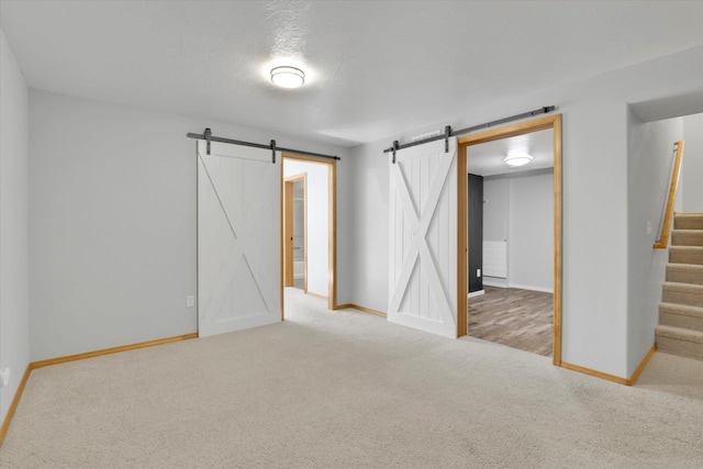 empty room featuring a barn door, carpet floors, and baseboards