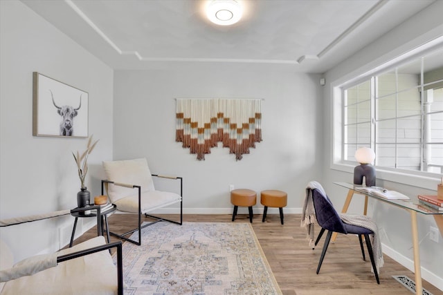 sitting room featuring wood finished floors, baseboards, and a tray ceiling
