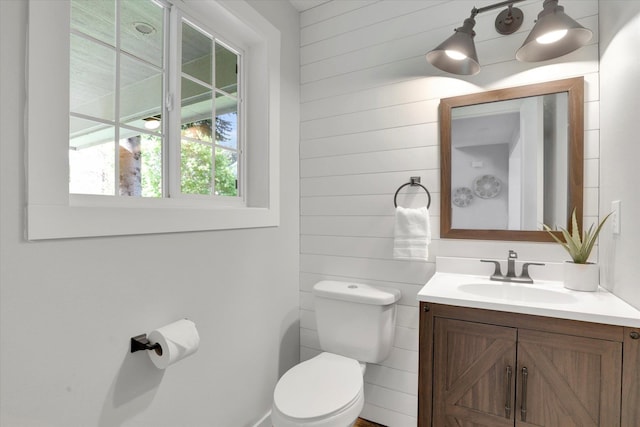 half bathroom featuring toilet, vanity, and wooden walls