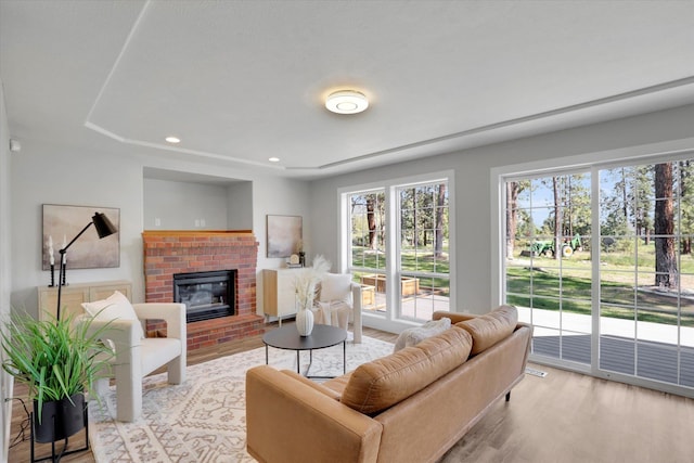 living area with light wood-style flooring, a brick fireplace, and recessed lighting