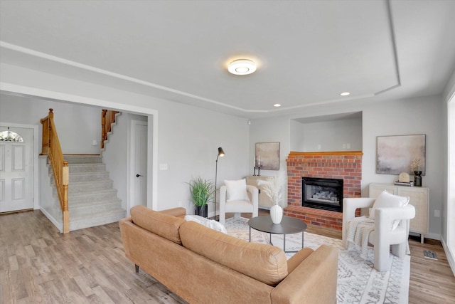 living area featuring light wood-style flooring, stairway, a brick fireplace, recessed lighting, and baseboards