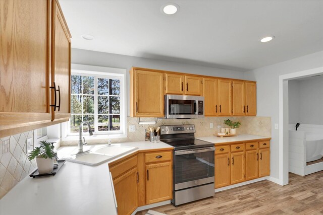kitchen with stainless steel appliances, a sink, tasteful backsplash, light countertops, and light wood-style flooring