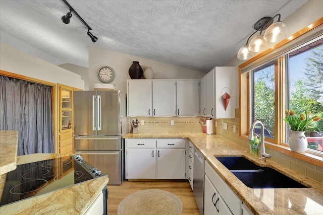 kitchen featuring stainless steel appliances, a sink, lofted ceiling, backsplash, and light stone countertops