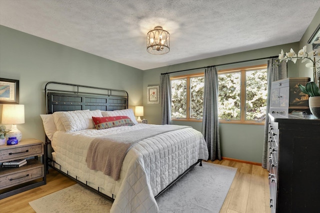 bedroom featuring light wood finished floors, a chandelier, a textured ceiling, and baseboards