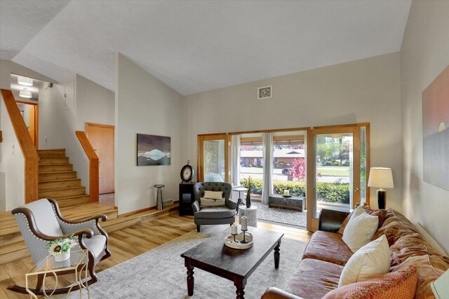 living room with light wood-type flooring, stairs, and high vaulted ceiling