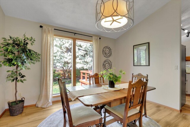 dining space with light wood finished floors, lofted ceiling, a chandelier, and baseboards
