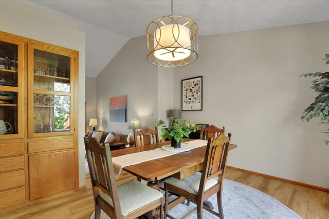 dining area with light wood finished floors, lofted ceiling, and baseboards