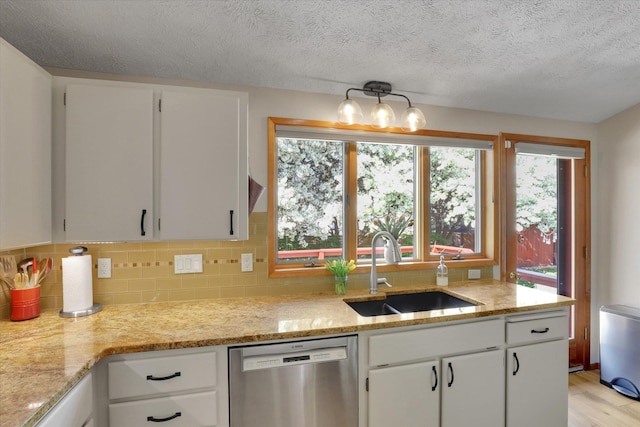 kitchen featuring stainless steel dishwasher, a sink, backsplash, white cabinets, and light wood-type flooring