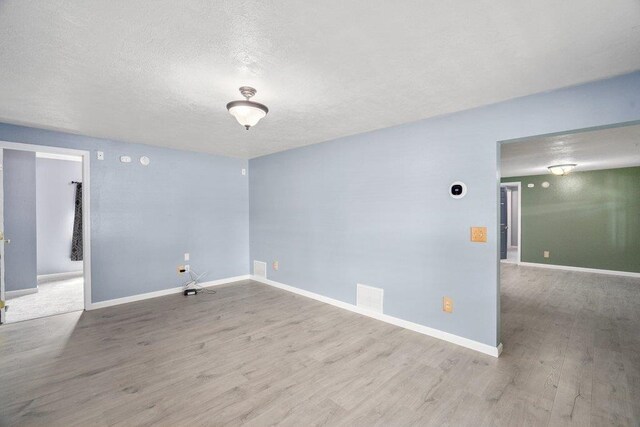 unfurnished room with wood finished floors, a textured ceiling, and baseboards