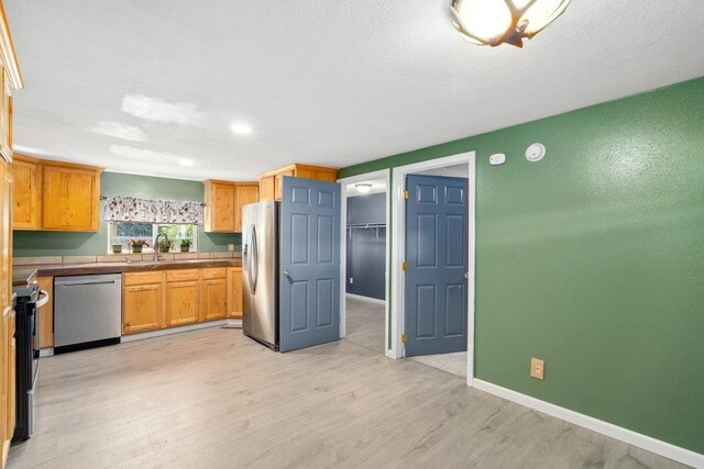 kitchen with stainless steel appliances, light wood-type flooring, baseboards, a sink, and recessed lighting