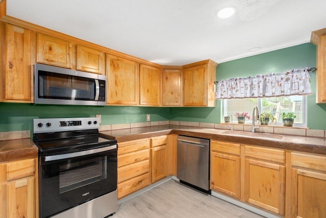 kitchen with appliances with stainless steel finishes, a sink, light wood finished floors, dark countertops, and recessed lighting