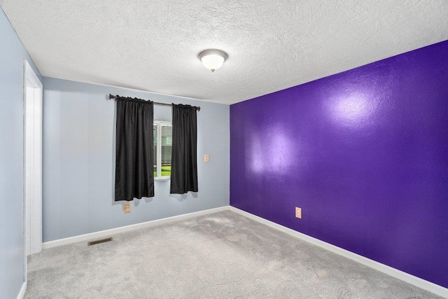 empty room with carpet, baseboards, and a textured ceiling