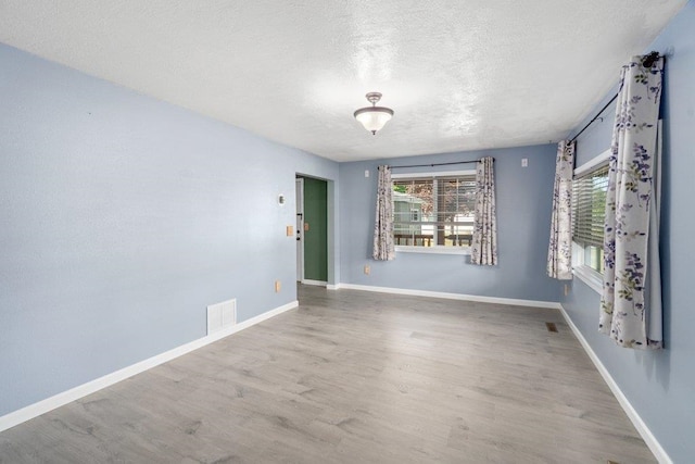 spare room with a textured ceiling, wood finished floors, and baseboards