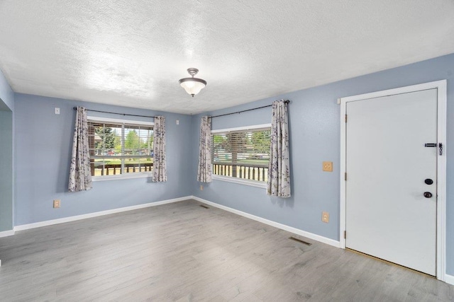 unfurnished room with a textured ceiling, wood finished floors, and baseboards