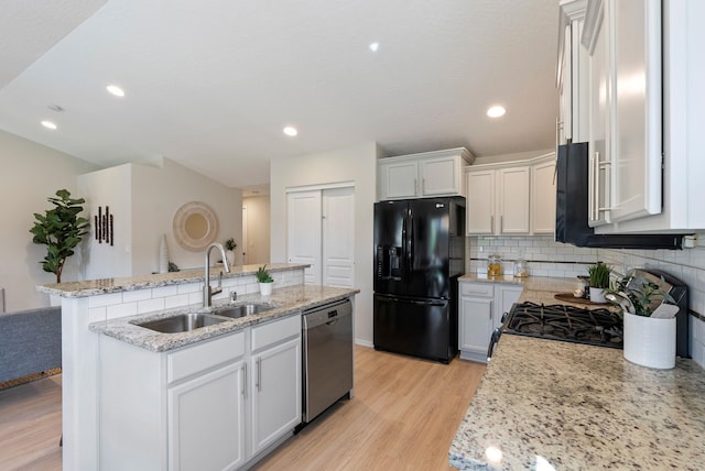 kitchen with black fridge with ice dispenser, stainless steel dishwasher, a sink, a center island with sink, and light wood-style floors