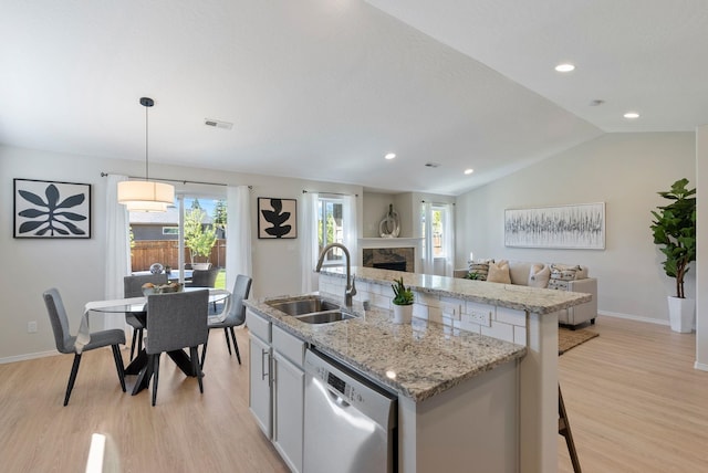 kitchen featuring dishwasher, a sink, light wood-style floors, a kitchen island with sink, and a fireplace