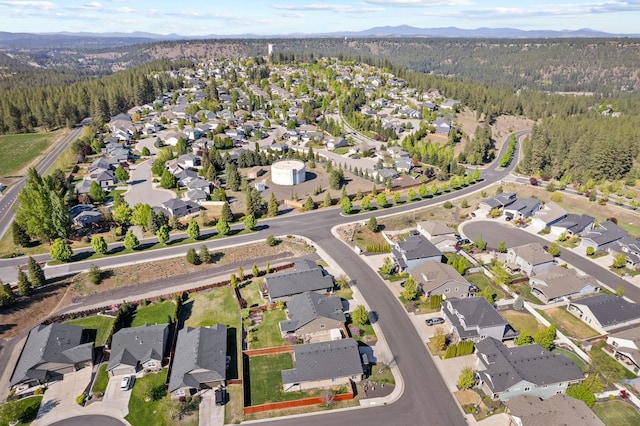 aerial view of property and surrounding area with a heavily wooded area, nearby suburban area, and a mountain backdrop