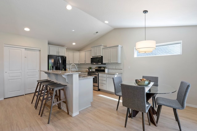 kitchen with stainless steel appliances, a breakfast bar, light wood-style flooring, backsplash, and lofted ceiling