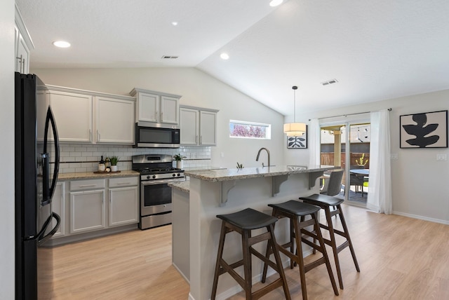 kitchen featuring appliances with stainless steel finishes, lofted ceiling, light wood-type flooring, tasteful backsplash, and a breakfast bar