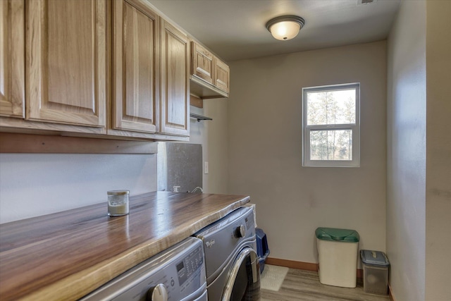 clothes washing area featuring washing machine and dryer, cabinet space, wood finished floors, and baseboards