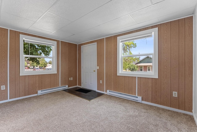 foyer with a baseboard heating unit, carpet floors, wood walls, and baseboards
