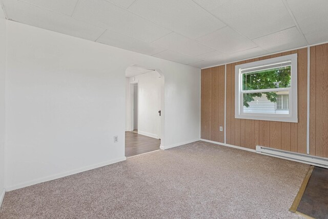 carpeted spare room with arched walkways, wood walls, baseboards, and a baseboard heating unit