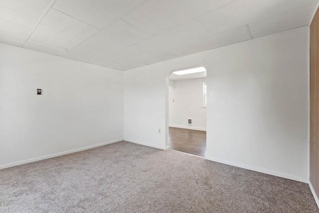 carpeted spare room featuring arched walkways, baseboards, and a paneled ceiling