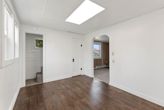 spare room featuring arched walkways, wood finished floors, a baseboard radiator, and baseboards