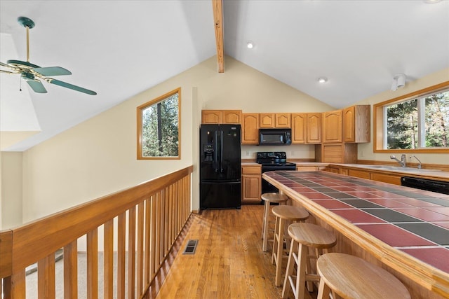 14512 N Dartford Dr, Spokane, WA 99208 - kitchen featuring black appliances, tile counters, a ceiling fan, light wood-style flooring, and a kitchen breakfast bar