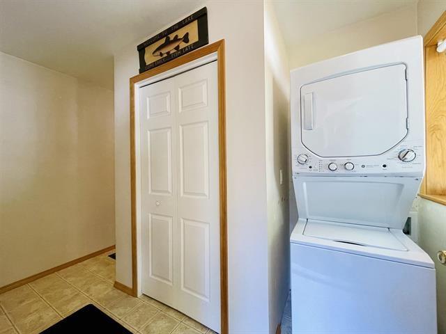 laundry room with stacked washer / dryer, baseboards, and light tile patterned floors