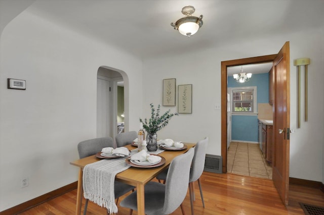 1308 W 11th Ave, Spokane, WA 99204 - dining room featuring arched walkways, a chandelier, baseboards, and light wood finished floors