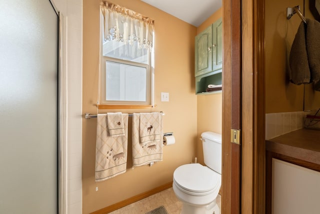 bathroom with toilet, a shower with shower door, and baseboards