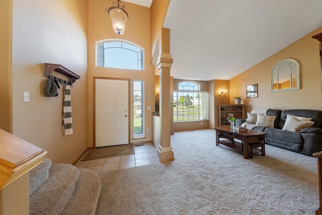 foyer with carpet flooring, tile patterned floors, ornate columns, baseboards, and high vaulted ceiling