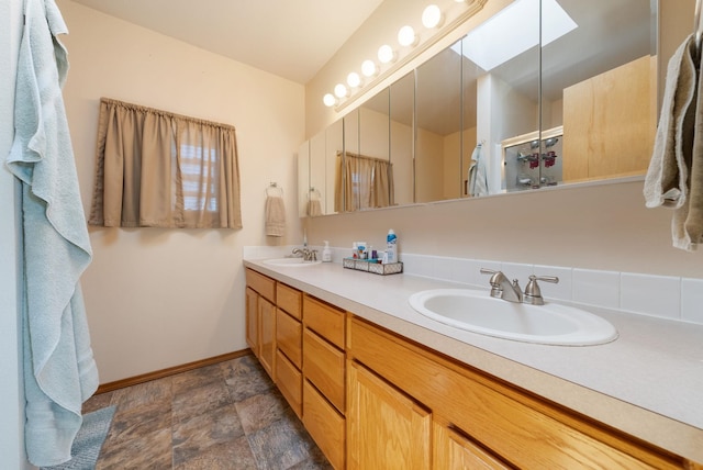 bathroom featuring baseboards, stone finish floors, double vanity, and a skylight