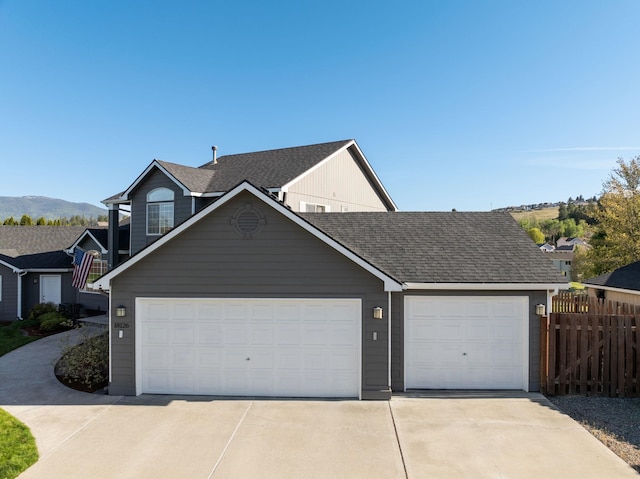 view of front facade featuring driveway, fence, roof with shingles, a garage, and a mountain view