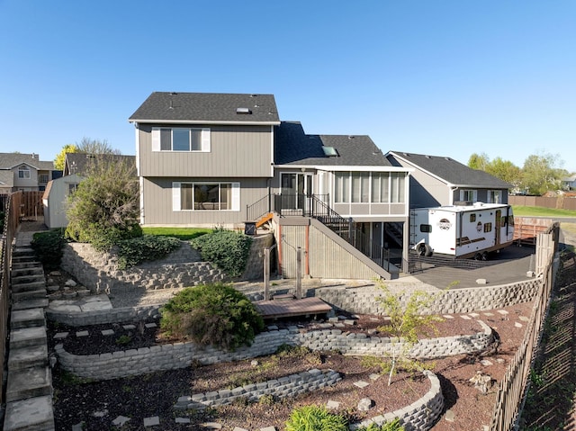 rear view of property featuring a sunroom, stairway, a residential view, fence, and roof with shingles