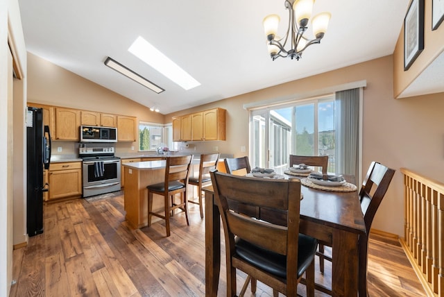 dining room with hardwood / wood-style flooring, a chandelier, a skylight, and high vaulted ceiling